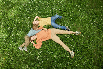 Wall Mural - Wide angle top view of mother and two children lying on green grass outdoors enjoying nature, copy space