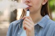 © New Africa - Young woman using electronic smoking device outdoors, closeup