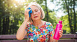 © NeuroCake - Mature woman suffering from a hot flash or heat exhaustion in a park, wiping her forehead. Menopause and summer heatwave health issues. Hydration concept