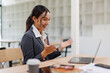 © David - Excited friendly young asian woman 20s in casual clothes sit on desk,  talk work on laptop pc computer get video call gesticulate in living room at workplace.