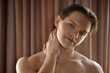 © Lustre Art Group  - A young man gently touches his neck, posing relaxedly against a soft brown curtain backdrop. Concept of tranquility and self-care in a serene environment.