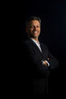 © Erik González - A man in a suit and tie is smiling and posing for a photo. He is wearing a watch and has his arms crossed. The image has a professional and confident mood