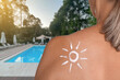 © New Africa - Woman with sun protection product on her shoulder by outdoor swimming pool, closeup