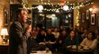 © Komang - StandUp Comedian Performing in Intimate Cafe Setting with Attentive Audience and Warm Lighting.