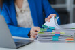 © Kritdanai - Workplace Documentation: A close-up shot of an office worker in a tailored blue blazer, meticulously reviewing a stack of documents.