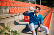 © Drazen - Male athlete drinking water while relaxing on staircase at stadium.