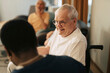 © Maskot - Smiling senior man sitting in wheelchair talking to male caregiver at retirement home