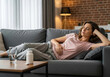 © Poetra RH - Woman experiencing abdominal pain while resting on a sofa at home, possibly due to stomach ache, menstruation, or indigestion. Ideal image for health, wellness, and medical-related content.