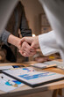 © Wasana - Two people shaking hands in front of a table with papers and a keyboard