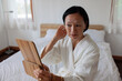 © Jovo Jovanovic/Stocksy - Woman in robe looks in mirror at her bedroom.