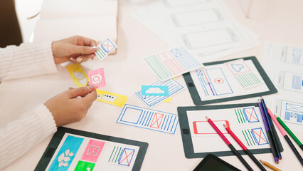 Wall Mural - ui ux designer asian woman hands creating mobile app wireframes on desk with colorful pencils, paper