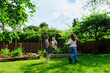 © BONNINSTUDIO/Stocksy - Happy children running in backyard vegetable garden with family