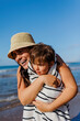 © BONNINSTUDIO/Stocksy - Mother embracing son wrapped in towel at beach on sunny day