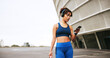 © peopleimages.com - Mobile, fitness and woman in city with music for exercise, streaming podcast or radio online. Phone, athlete and listening to headphones outdoor for workout audio, mockup space and walking with bag