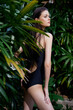 © SHOTPRIME STUDIO - Attractive young woman in black swimsuit posing against lush green foliage in tropical garden