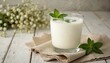 © Raisa - Traditional Turkish ayran drink in glass with mint garnish. Yogurt based beverage on beige napkin, white wood table. Healthy probiotic dairy drink, cold refreshment.