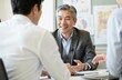 © Raisa - Mature asian businessman meets with colleagues in office. Senior man in suit smiles during corporate meeting. Gray hair executive shares expertise. Successful entrepreneur looks confident, explains