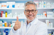 © Raisa - Happy mature male pharmacist shows thumbs up in pharmacy. Doctor smiles at camera. Pro health worker stands near shelves with medicines, equipment. Man supports healthcare, pharmaceutical supplies.