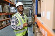 © Serhii - Portrait african warehouse supervisor standing large warehouse distribution center with colleague worker in background. Business warehouse and logistic concept