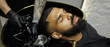 © Dmytro Hai - Web banner of tattooed barber holding faucet near sink and african american client in barbershop