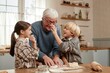 © Seventyfour - Senior Caucasian man smiling while preparing dough with two children in kitchen, girl and boy laughing and interacting with grandfather during baking activity in village home