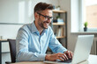 © Pete - Smiling businessman works on laptop. Man typing on computer in office doing research project. Happy employee, professional, corporate worker smiles. Digital tech, online, data, business, finance.