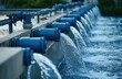 © dreamer - Multiple blue industrial pipes discharge water into a treatment or filtration system channel outdoors.