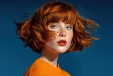 Close-up portrait of a young woman with vibrant red hair and blue eyes wea orange top against dark blue background