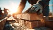 © standret - Close up of mason placing bricks with sunlight in background