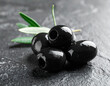 © JBN - Fresh black olives on a dark stone surface with olive leaves nearby