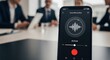 © Dmitry - A man holding a phone with an active voice recording app over a blurred business meeting. Cyber surveillance concept.