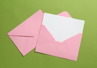 Wall Mural - Blank invitation card and envelopes on green background, flat lay. Space for design