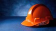 © Stockify Pro - A vibrant orange construction helmet rests on a deep blue textured surface, showcasing its design aimed at ensuring safety in construction and industrial activities