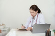 © Ekkasit A Siam - Female orthopedic doctor writing notes on clipboard while observing symptoms of joint pain in elderly asian patient during clinical consultation, preparing treatment plan with professional focus
