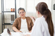 © Ekkasit A Siam - Orthopedic doctor speaks to senior asian woman in wheelchair about treatment plan for chronic bone and joint pain, with both seated across desk in modern clinic filled with natural light