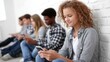 © SerPak - Group of diverse teens engaged with smartphones against brick wall.