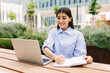 © Xavier Lorenzo - Young woman working on laptop sitting outdoors. Millennial female student studying online sitting on campus bench. Education and business concept.