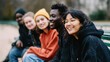 © dinatychynska - A diverse group of teenagers from different ethnic backgrounds sitting on a bench in a park, representing youth, friendship, diversity, and unity, showcasing modern society and cultural connections.
