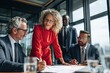 © amaf - A diverse business team collaborates around a table, reviewing documents; a woman in red leads the discussion in a modern office setting