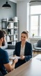© soysuwan123 - A professional woman smiling and handing a notebook to a man during a casual office meeting in a modern workspace.