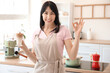 © Pixel-Shot - Young woman with glass of iced latte showing OK in kitchen