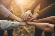 © jendralbiribiri - Diverse team joining hands shows collaboration, unity, and strength, illuminated by warm sunlight, representing partnership and success in achieving common goals.