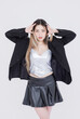 © Bangkok Click Studio - Fashion asian pretty young woman model pose playfully confident wearing silver corset top black pleated leather skirt black jacket expressing trendy streetwear style creative against white background.