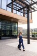 © Bogdan Pictures - A confident professional dressed in a stylish navy suit walks briskly outdoors next to a contemporary office building, energetically making a phone call while engaging with their busy workday