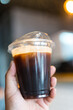 © Dontree - Hand holding iced black coffee or americano coffee in plastic cup, against bokeh background