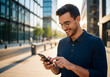 © SenpaiNoticeMe - Happy young man smiles while using his smartphone outdoors in a modern city setting.