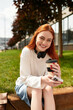 © Bliss - Young woman enjoys her spare time with coffee and laughter in a sunny park