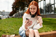 © Bliss - Relaxing outdoors, a young woman enjoys sipping coffee while scrolling on her phone