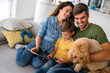 © NDABCREATIVITY - Joyful Caucasian family spending time together with digital devices and dog at home.