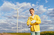© Iryna - Smiling teenage boy in yellow jacket holds wind turbine model with solar panel on open field with real turbines. Concept of environmental education, rural energy research, climate awareness.